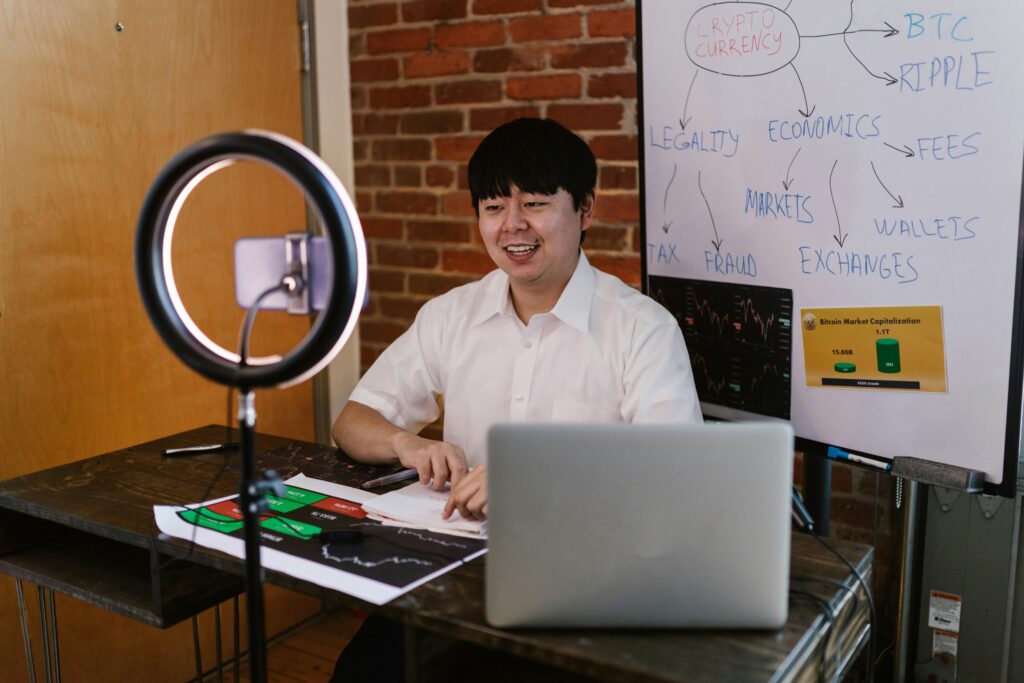 pexels-photo-8369655-8369655 Man discussing cryptocurrency economics with ring light and laptop, engaging content creation.